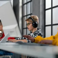 Drie jonge kinderen zitten in een klaslokaal achter computerschermen.