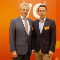 Johan en Tom Willemen van de gelijknamige bouwgroep, beiden in kostuum, op de nieuwjaarsreceptie (2018) van VOKA, tegen een oranje achtergrond.