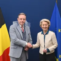 Bart De Wever en Ursula von der Leyen schudden elkaar de hand voor een Belgische en Europese vlag.